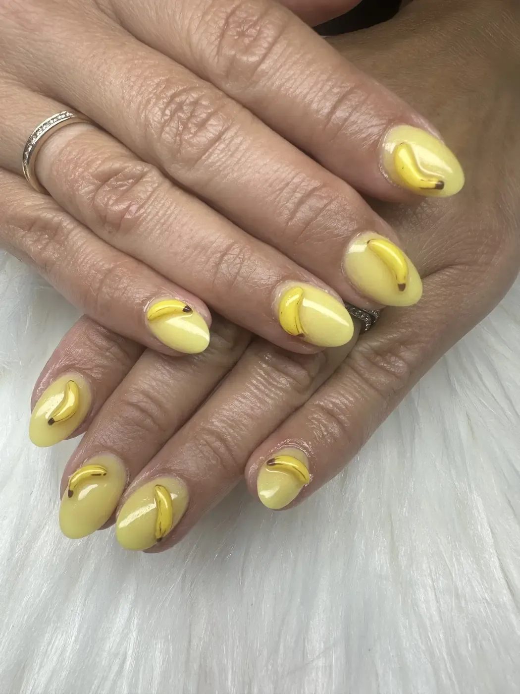 Playful 3D banana nail art on a pastel yellow set at Nails Trend
